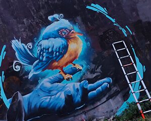 Eisvogel auf einer geöffneten Hand als blaues Wandbild an einer Außenfassade